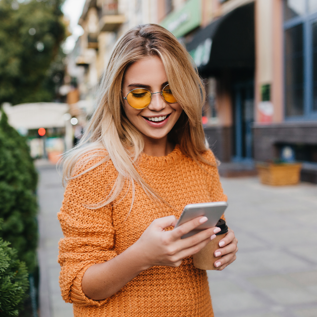 Person holding a smartphone and coffee cup on a city sidewalk